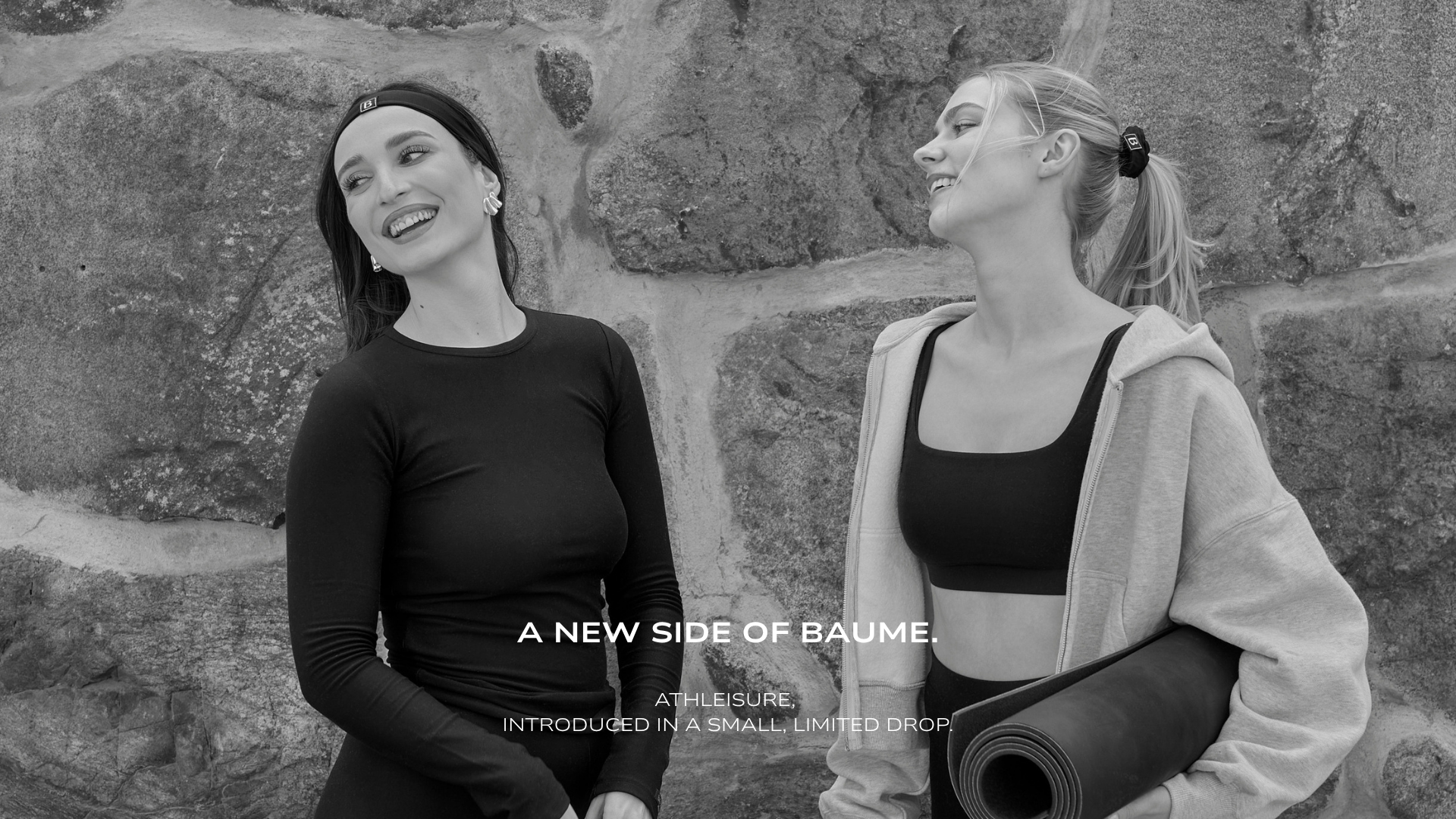 Two women laughing together on the street, wearing BAUME Essentials athleisure from the Form Collection. One wears a long-sleeve top and tights, while the other wears shorts and a bralette. Minimal, versatile everyday clothing made from TENCEL™ Lyocell and responsibly made in Portugal.