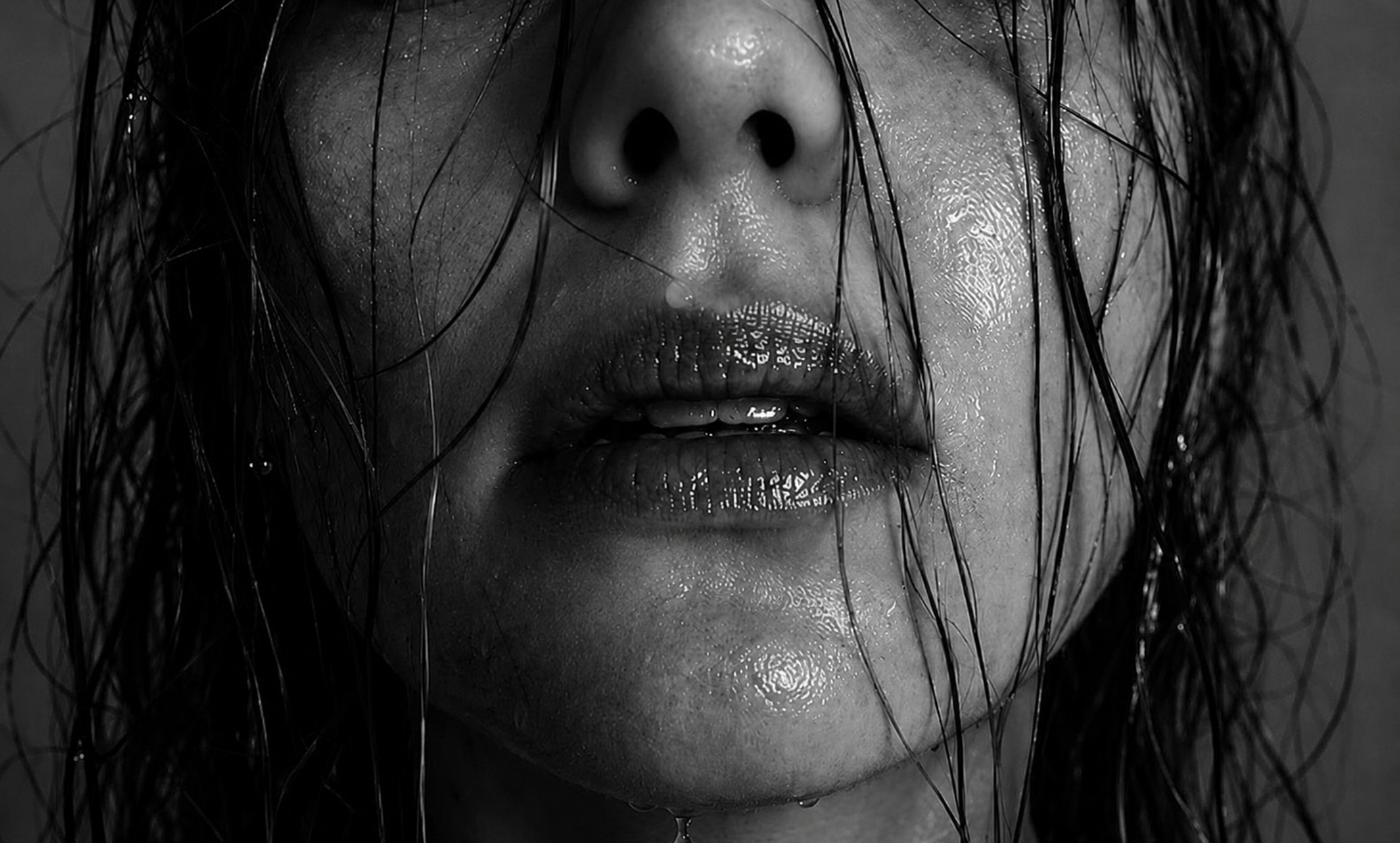 Close-up of a person's face with wet hair and shiny lips in black and white.