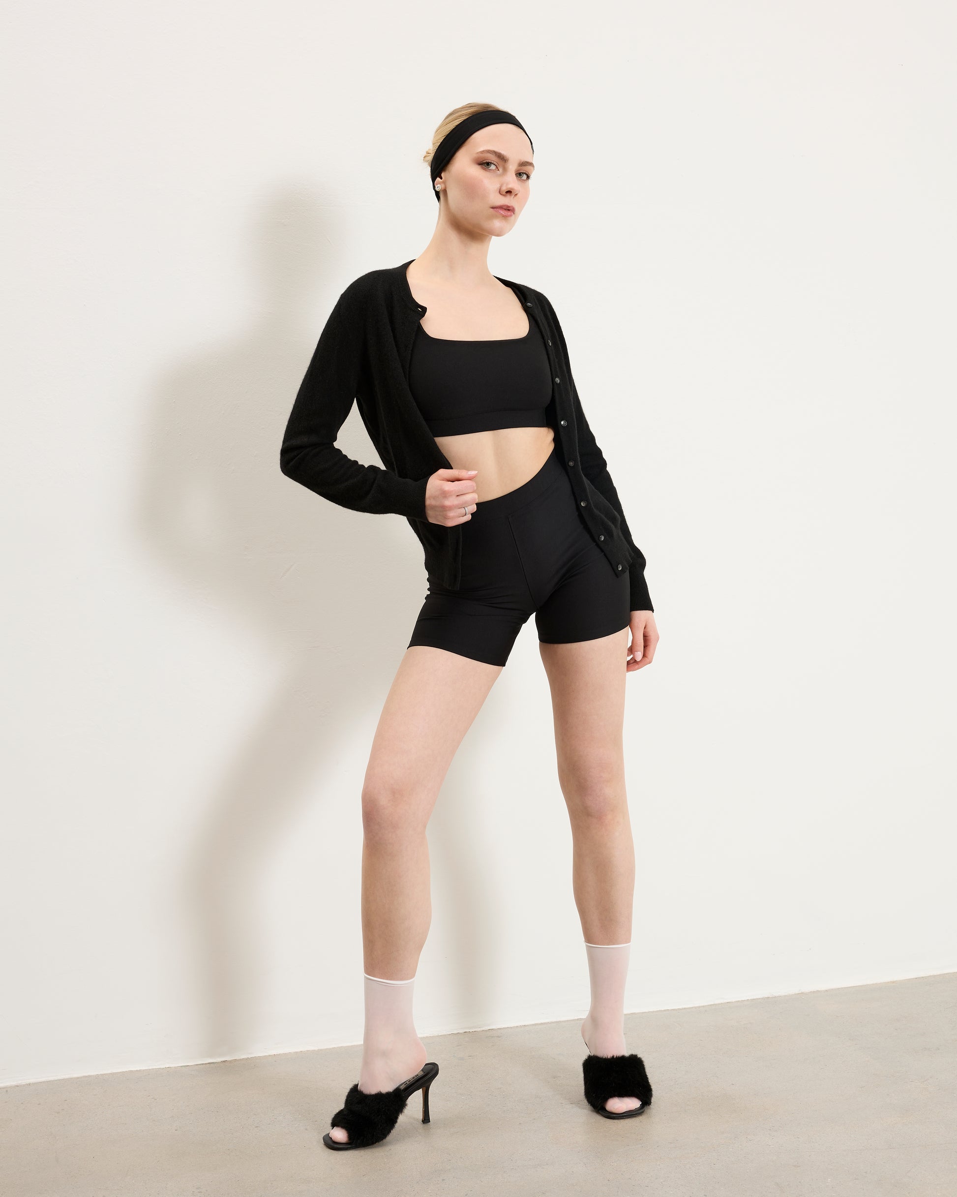 Woman wearing Baume Essentials Atleisure bralette and shorts styled with cardigan, heels and accessories for a versatile everyday look.