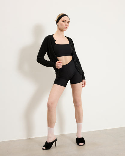 Woman wearing Baume Essentials Atleisure bralette and shorts styled with cardigan, heels and accessories for a versatile everyday look.