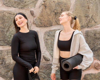 Two women wearing Baume Essentials Atleisure TENCEL™ Lyocell loungewear sets, made from soft breathable and sustainable materials, sharing a relaxed everyday moment by a wall.