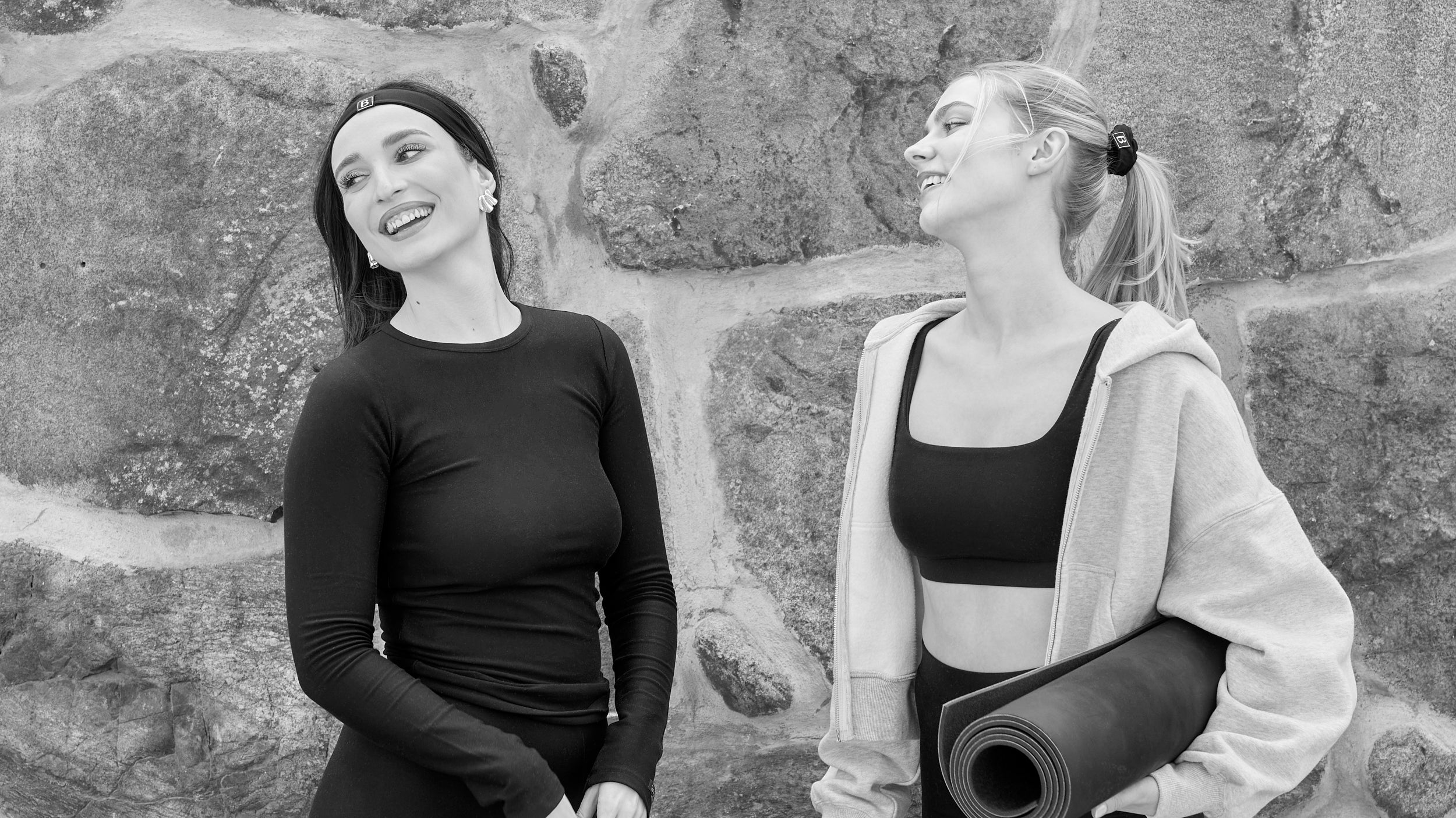 Two women wearing Baume Essentials Atleisure TENCEL™ Lyocell loungewear sets, made from soft breathable and sustainable materials, sharing a relaxed everyday moment by a wall.