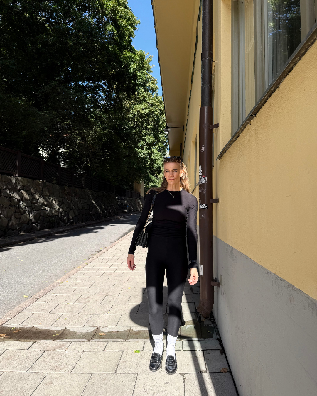 Woman wearing a black BAUME long-sleeve top and leggings, styled as versatile everyday layers for a capsule wardrobe.