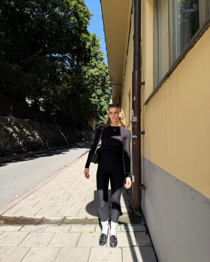 Woman wearing a black BAUME long-sleeve top and leggings, styled as versatile everyday layers for a capsule wardrobe.