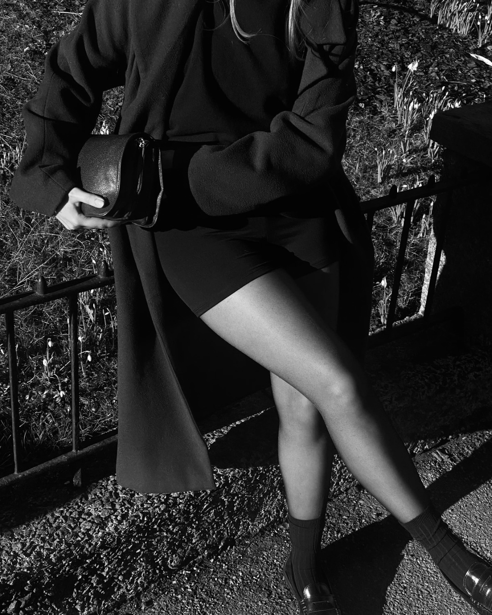 Woman wearing BAUME Essential 03 Shorts with stockings, a knitted sweater and long coat, styled with a bag for an elevated layered everyday outfit.