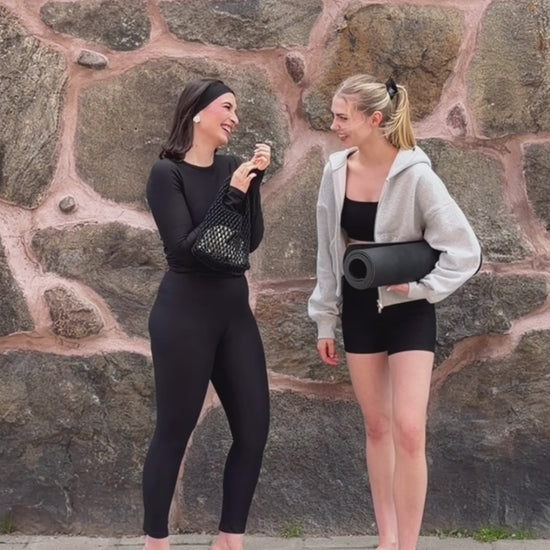 Two women wearing BAUME Form black tights, long-sleeve top, bralette and shorts, styled from elevated with heels and accessories to relaxed with a hoodie and flip flops.