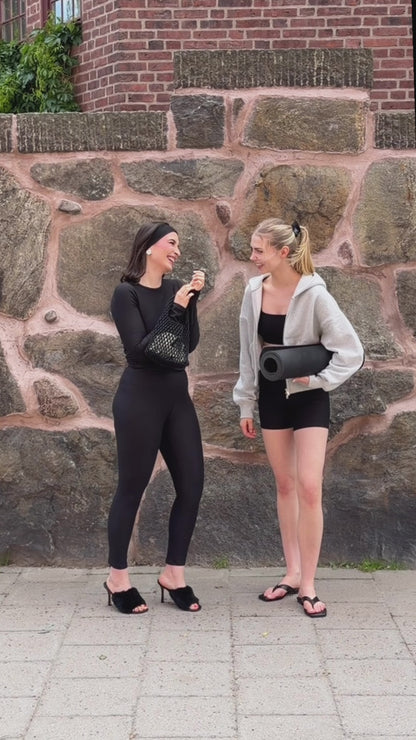 Two women wearing BAUME Form black tights, long-sleeve top, bralette and shorts, styled from elevated with heels and accessories to relaxed with a hoodie and flip flops.