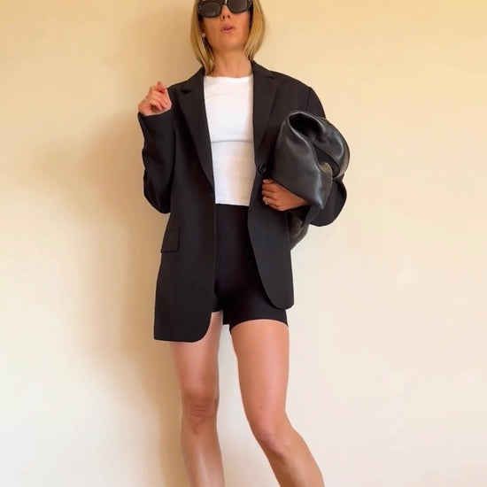 Woman wearing BAUME Form Bralette and Shorts with a T-shirt, blazer and heels, showing versatile activewear styled for an elevated workwear look.